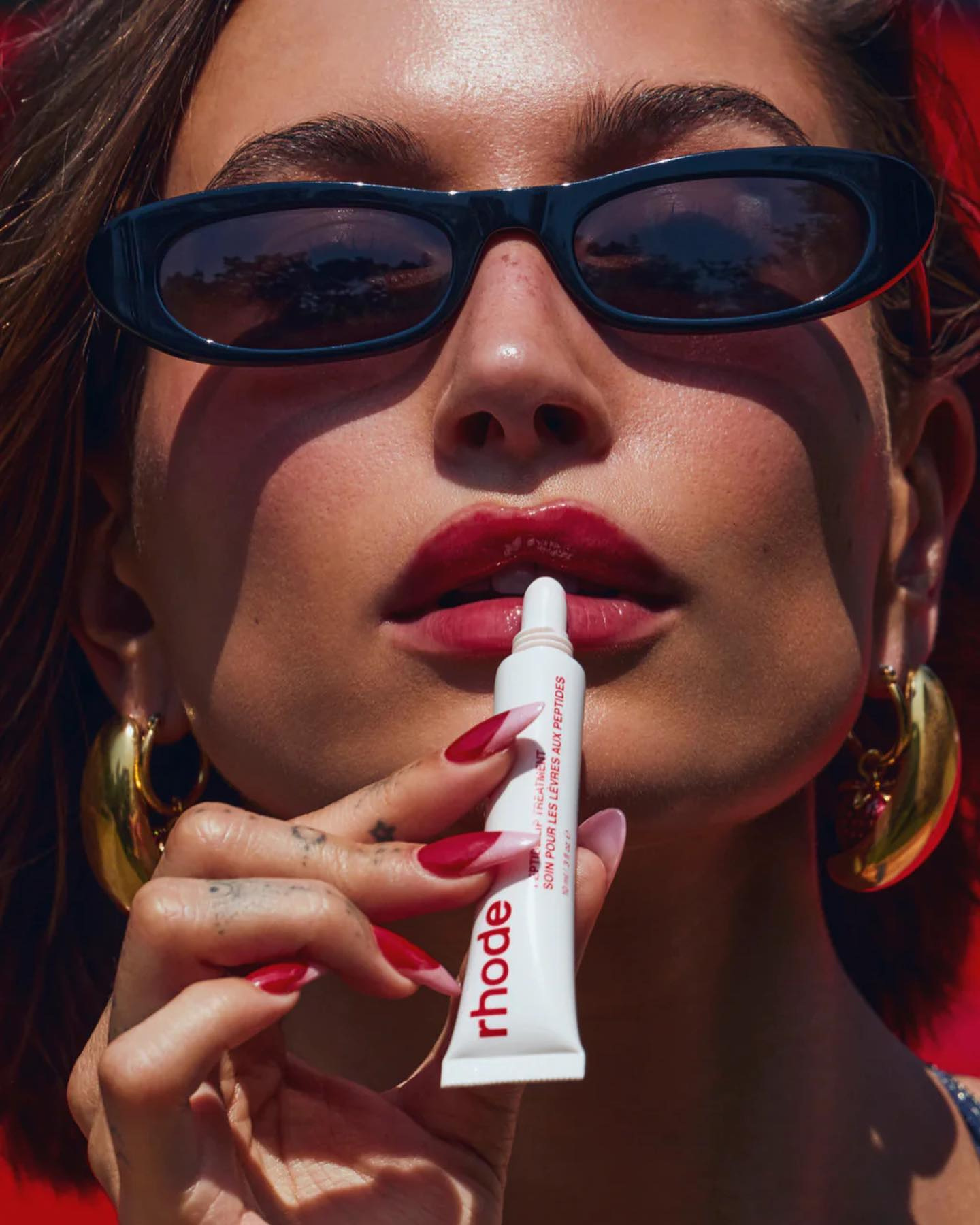 Hailey Bieber applying Rhode lip treatment.